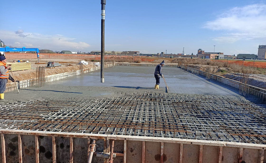 Cantiere con operai per realizzazione di hangar di manutenzione, linee di volo, polo tecnologico, centrali elettriche